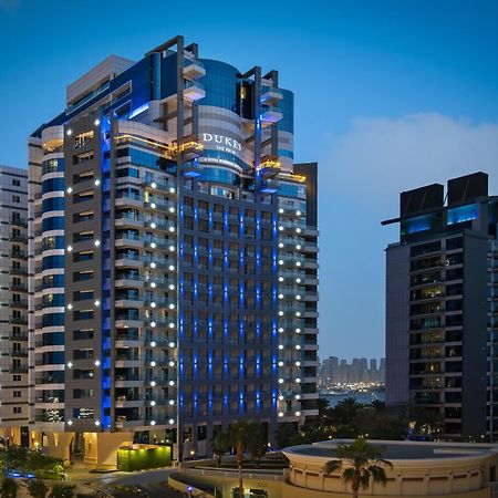 Dukes The Palm, A Royal Hideaway Hotel Dubaj Zewnętrze zdjęcie The photo shows a modern high-rise building, which appears to be a hotel or residential complex. The design features sleek lines and a glass façade, illuminated with blue lighting that enhances its contemporary look. Surrounding the main building are