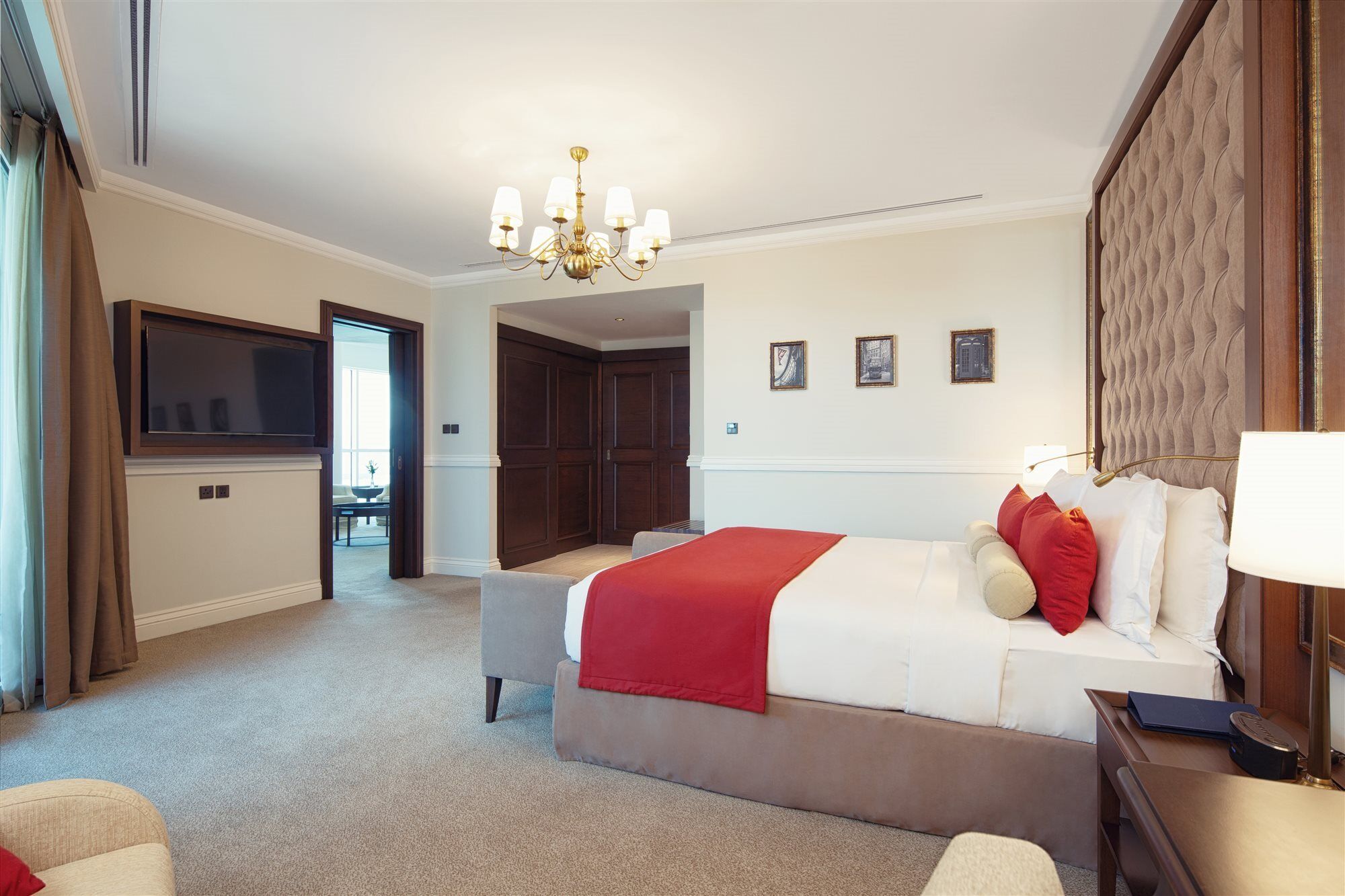 Dukes The Palm, A Royal Hideaway Hotel Dubaj Zewnętrze zdjęcie The photo shows a well-appointed hotel room. It features a large bed with white linens and red accent pillows. There is a comfortable seating area with a chair, and a side table. A chandelier hangs from the ceiling, providing lighting. On the wall be